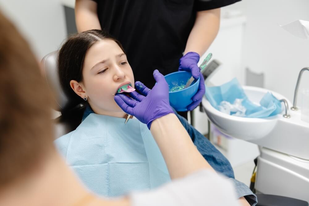 A woman sits in a dental chair while a dentist cleans her teeth, demonstrating the process of dental sealants.
