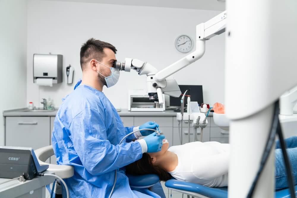 A dental professional in scrubs uses specialized equipment while attending to a patient in a modern clinic setting.