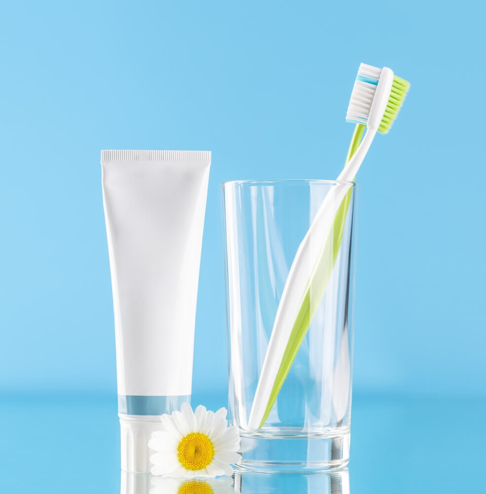 Toothbrush and toothpaste beside a glass of water on a vibrant blue background, ready for a refreshing dental routine.