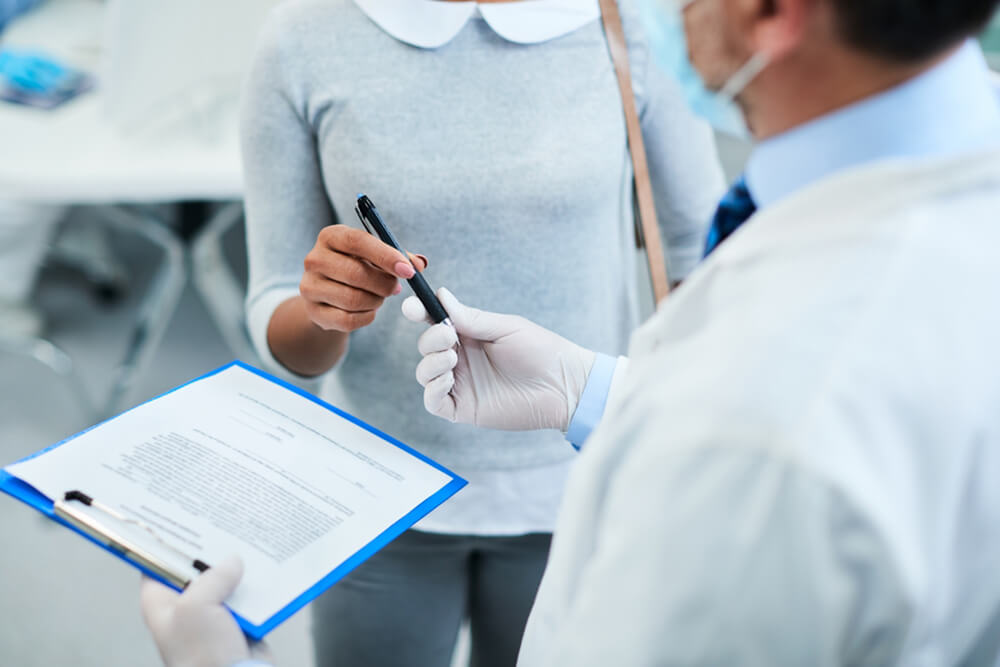A doctor holds a clipboard while a woman attentively reviews the information, highlighting insurance and accessibility concerns.