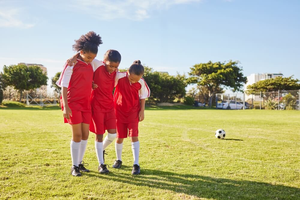 Three young athletes in red soccer uniforms stand proudly on a field, embodying the enthusiasm of youth sports participation.