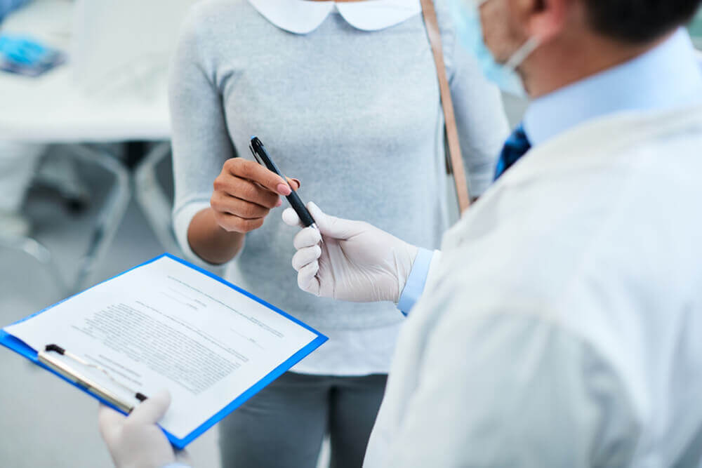 A doctor holds a clipboard while a woman attentively reviews the information, highlighting insurance and accessibility concerns.