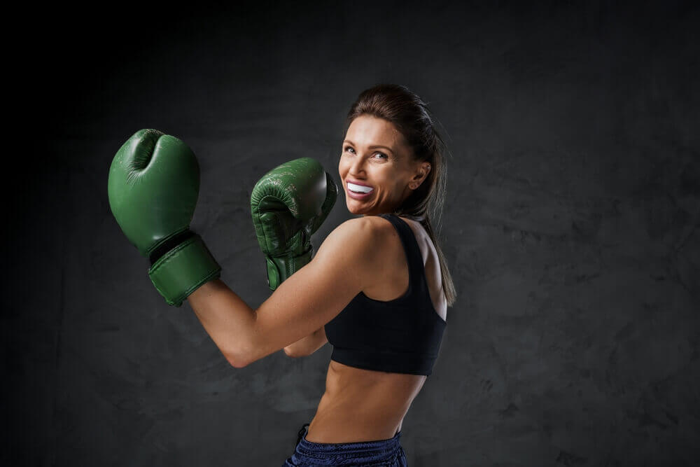 A woman in boxing gear raises her hands in a fighting pose, emphasizing her Sports Guards and athletic readiness.